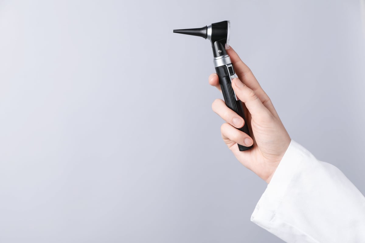Doctor with otoscope on light grey background, closeup. Space for text