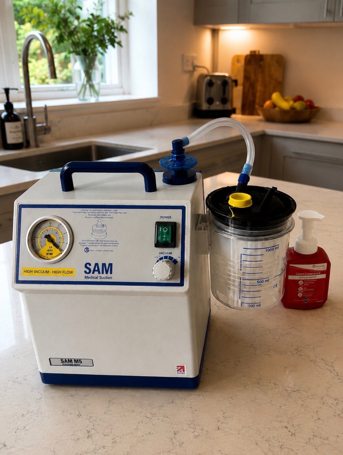 SAM medical suction machine on kitchen countertop with collection canister and tubing attached, next to red bottle