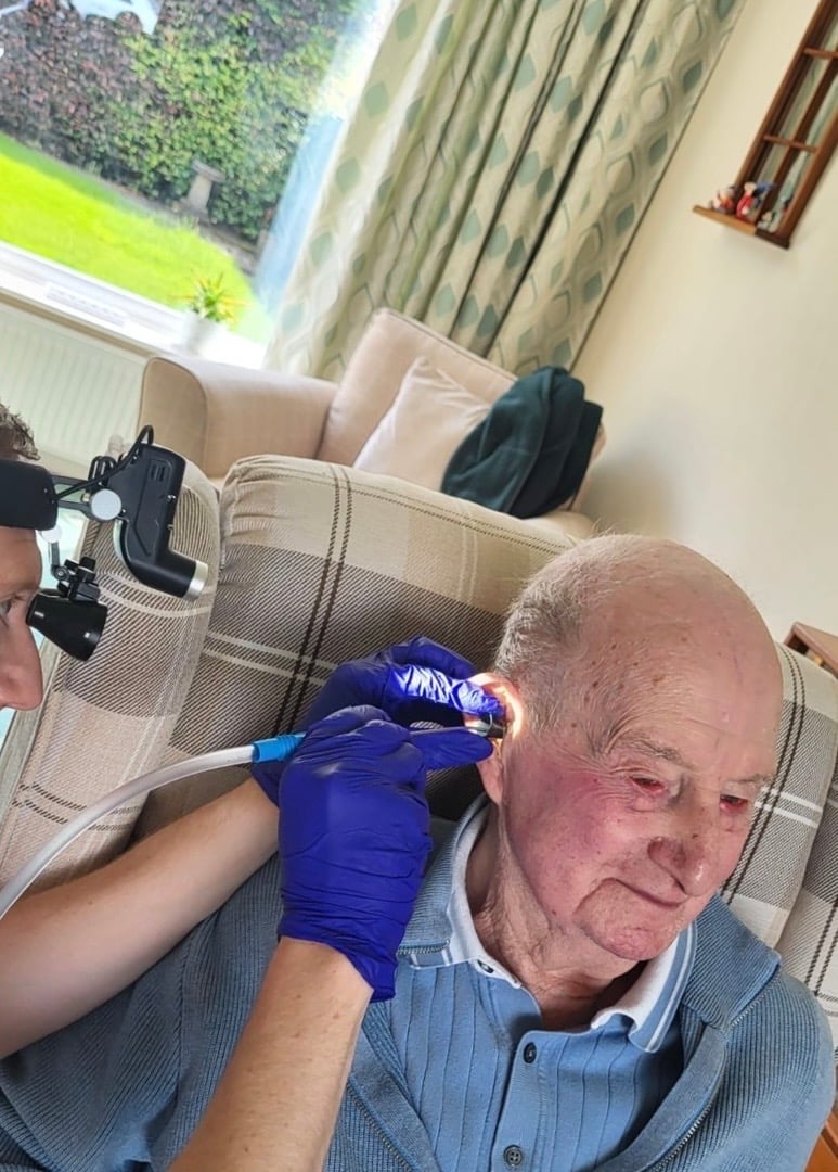 Medical professional applying treatment to senior mans scalp while another person operates a camera in a home setting